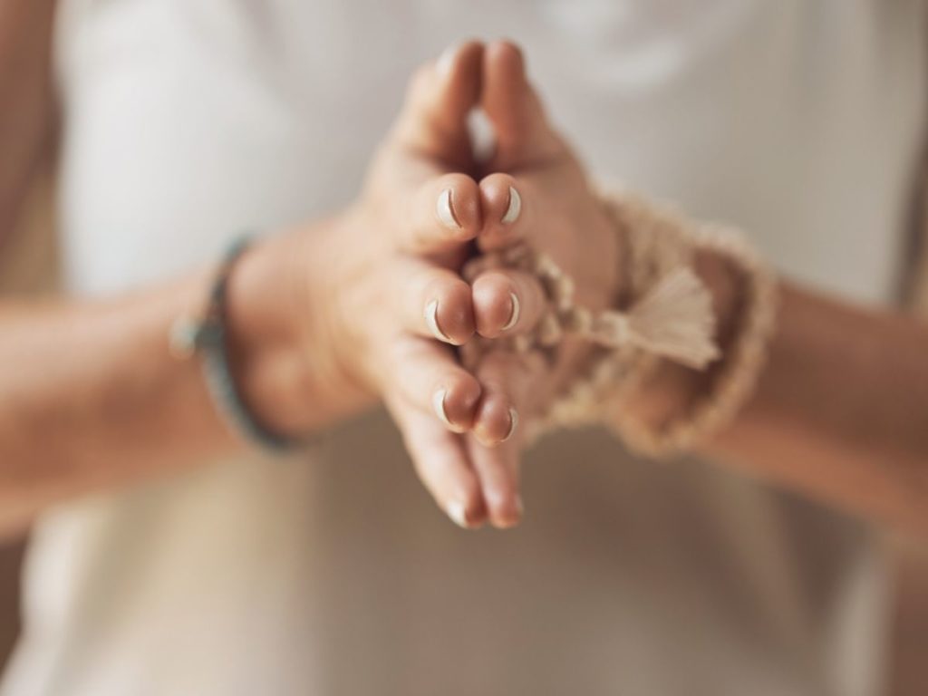 Woman with her hands together in the prayer position while engaging in somatic therapy for anxiety in Los Angeles. Woman is wearing a white shirt, face not shown.