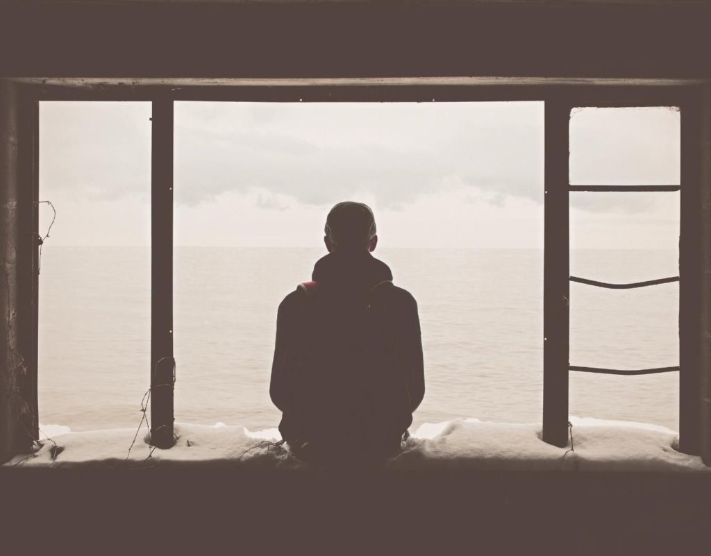 Man in Los Angeles looking out window. Black silhouette sitting on bench, man looking for holistic trauma therapy in Los Angeles