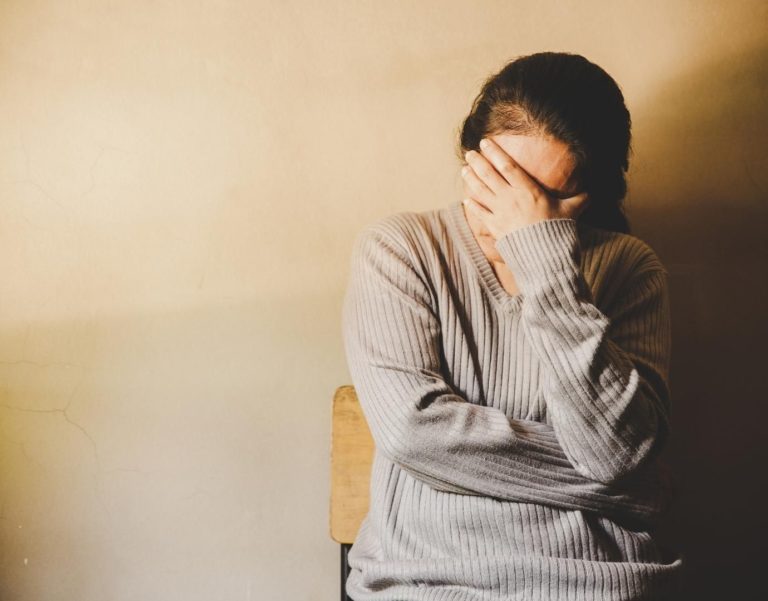 Woman getting complex-ptsd therapy in los angeles office. yellow walls, woman in gray shirt with hand over face.