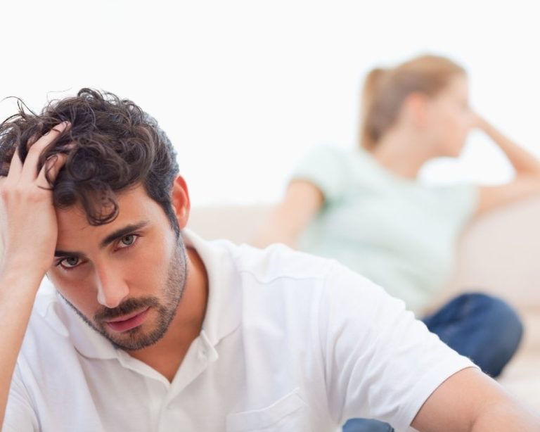 A couple in an argument in an attachment therapy session in LA, illustrating communication in therapy. Couch is gray, both people wearing white shirts and the background is white