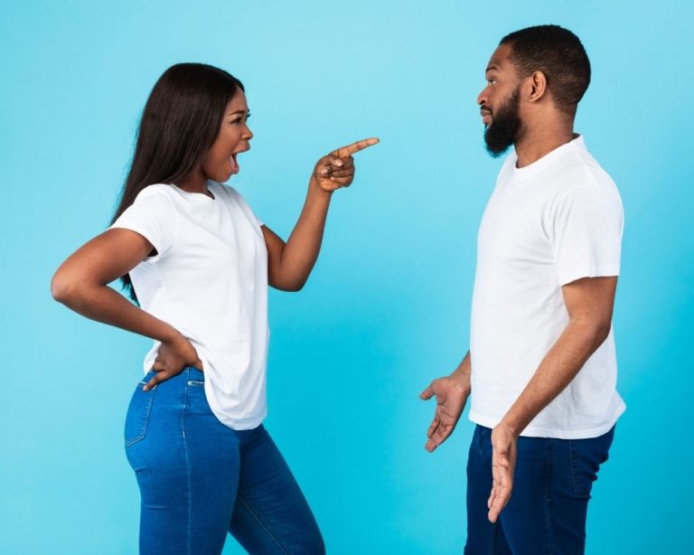 A couple in an argument in an attachment therapy session in LA, illustrating communication in therapy. Couch is gray, both people wearing denim jeans and looking angry. background is light blue