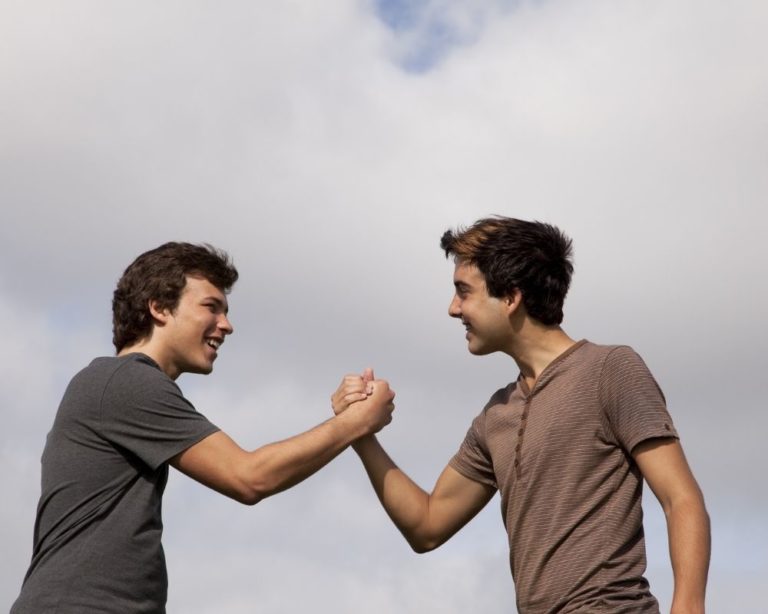 Two men shaking hands out of achievement in Los Angeles. Men are celebrating healing in trauma therapy and are smiling. Blue sky and clouds in background