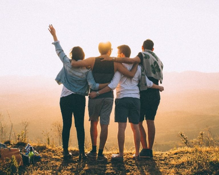 Group of friends in Los Angeles looking out towards sunset. 4 friends with back towards camera and holding each other after attachment therapy