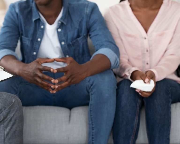 A couple in an argument in an attachment therapy session in LA, showing that communication in therapy can help couples and relationships. Couch is gray, both people wearing denim jeans and the photo does not show their faces.