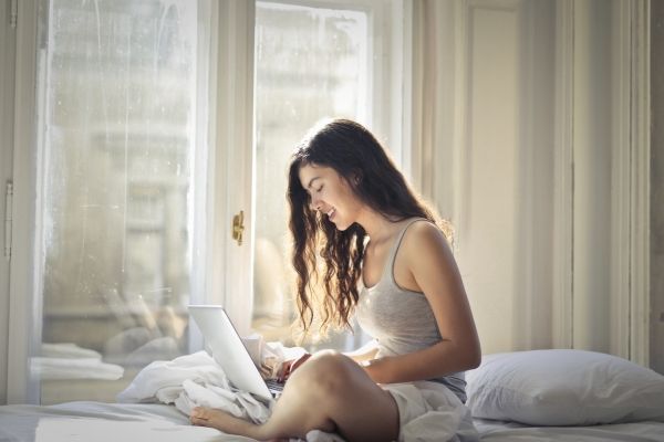 Woman relaxing in a Los Angeles room. There are white curtains, white sheets, and woman doing somatic therapy work on bed.