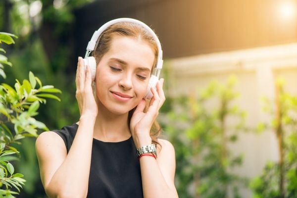 Woman walks outside listening to music and sounds in Los Angeles. Woman is practicing somatic therapy to heal from complex PTSD, wearing headphones, and black shirt.