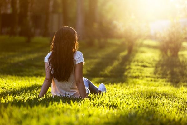 A woman practicing somatic therapy breathing exercises to heal from complex ptsd in a quiet Los Angeles park, surrounded by lush greenery.