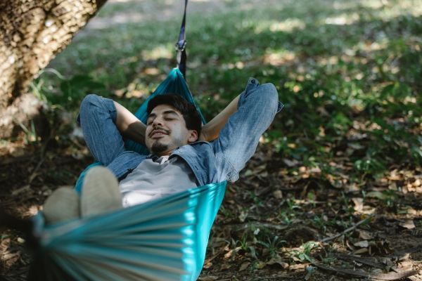 Man in Los Angeles park relaxing in his body as somatic therapy practice to help treat PTSD. Man is in green lush park wearing blue.