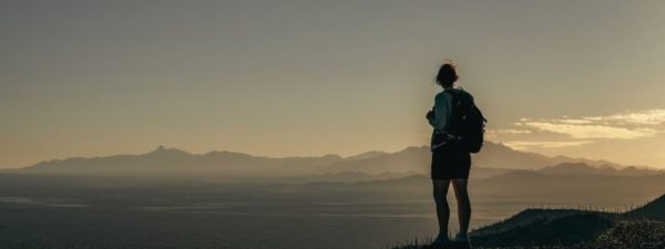 Person overlooking Los Angeles cliff at sunset. Shows an individuals shadow from the back, wearing a backpack.