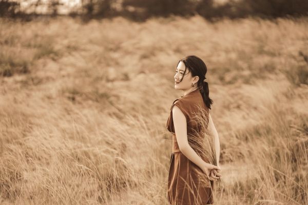 Woman standing in a field in Los Angeles for trauma therapy. Field is full of brown brushes, and woman is wearing brown dress with hands behind back.