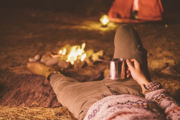 Person relaxing on the ground while camping, drinking coffee, and enjoying nature.