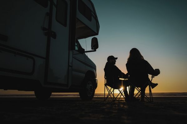 Two people sitting on camping chairs near a camper in Los Angeles during sunset.