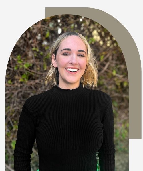 Holistic anxiety & attachment therapist in Los Angeles, Cheryl Groskopf, LMFT, LPCC laughing in front of bushes. She has a warm smile and is laughing wearing a black shirt and green bushes in the background.