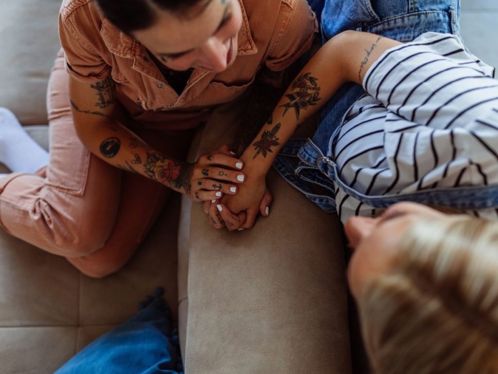 Two women holding hands on a couch, showing their love and affection with each other through attachment therapy in Los Angeles.