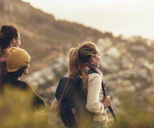 Man and woman friends walking in a somatic hike in Los Angeles as part of holistic therapy. Woman has backpack and ponytail, friend has beanie, and man is looking off at distance.