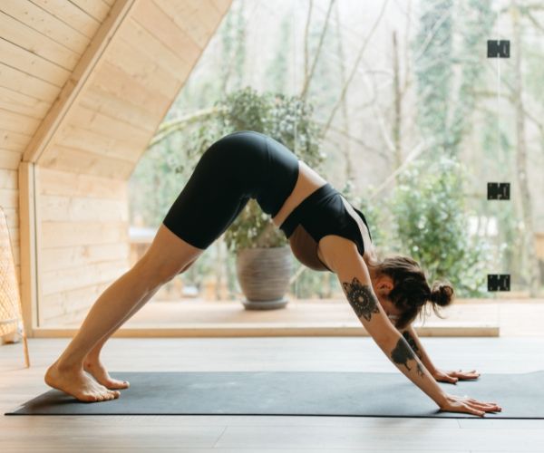 Woman with tattoos practicing downward dog yoga pose during a somatic therapy session in Los Angeles.