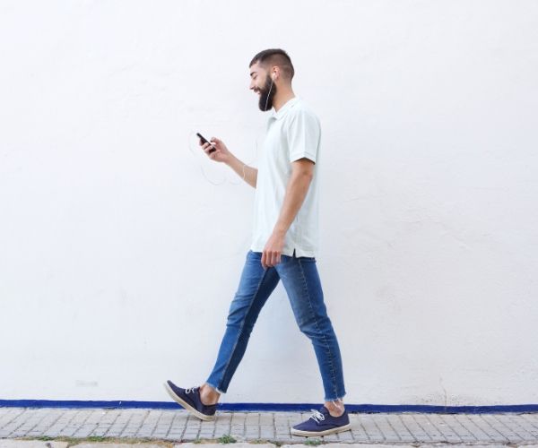 Man walking outdoors with headphones and looking at his phone, symbolizing mindful movement used in somatic therapy in Los Angeles