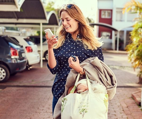 Smiling woman with a tote bag and phone, symbolizing personal empowerment and growth through trauma therapy in Los Angeles