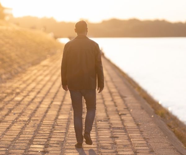 Man walking along a riverbank at sunset, symbolizing reflection and emotional healing in trauma therapy Los Angeles