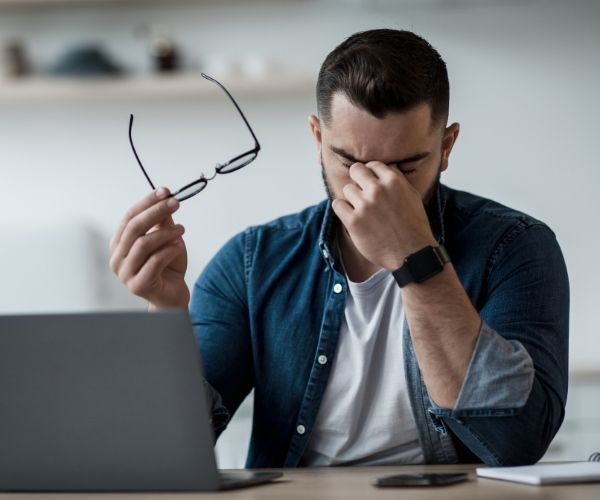 Frustrated man holding glasses at his desk, representing the emotional challenges addressed in trauma therapy in Los Angeles.