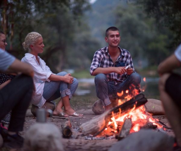 A group of people sitting by a campfire near the ocean, symbolizing connection, grounding, and healing through somatic and trauma therapy in Los Angeles.