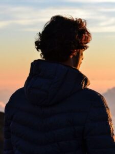 Man in a hooded jacket watching the sunset, symbolizing reflection and resilience in trauma therapy, Los Angeles.