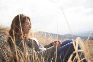 Woman sitting in a serene Los Angeles field, deep in thought—representing self-reflection, healing, and trauma therapy through somatic approaches for anxiety relief