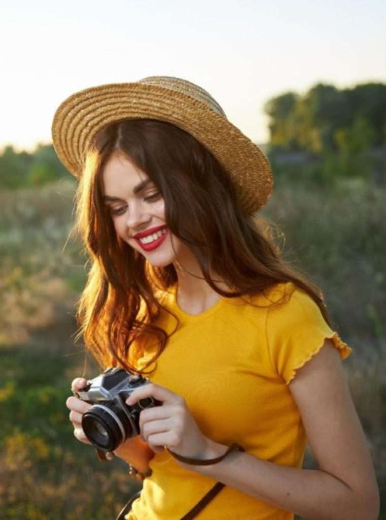 woman in los angeles, california taking photos with her camera. woman is wearing yellow shirt and hat.