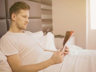 Man enjoying a book in bed, reflecting on somatic therapy and personal growth in Los Angeles.