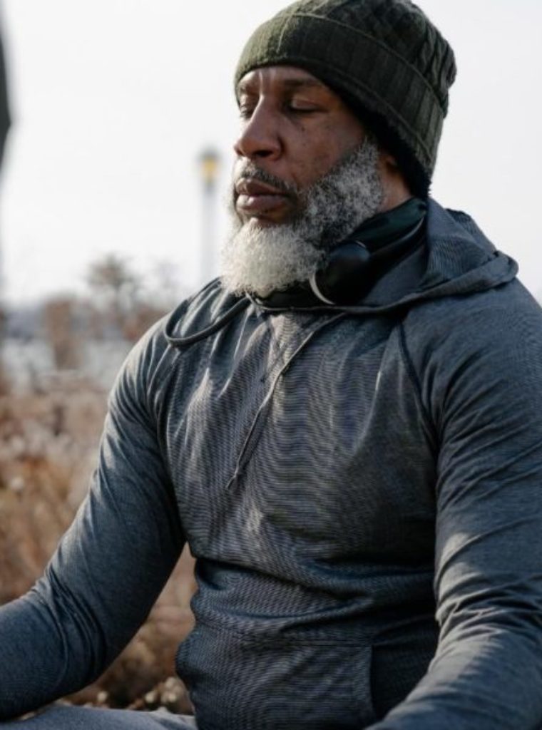 Man in Los Angeles meditating when receiving attachment therapy. Man is wearing grey sweater, eyes closed, beanie, and looks calm.