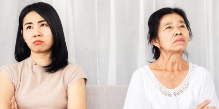 Adult Child of Narcissistic parent: narcissistic mother sitting with adult child daughter, both are cold and distant, not looking at each other with arms crossed, white shirts, white background