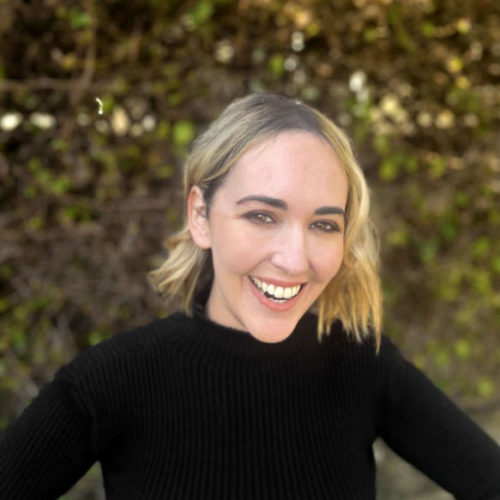 Photo of holistic therapist Los Angeles, Cheryl, smiling with black shirt in front of a green bush