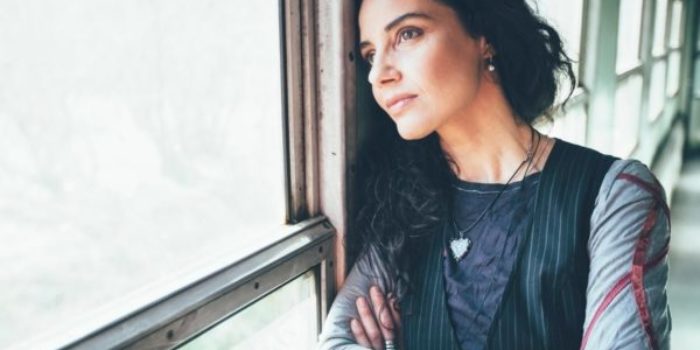 Woman with black hair looking out window, wondering what to expect in therapy. Woman wears black shirt and bracelet.